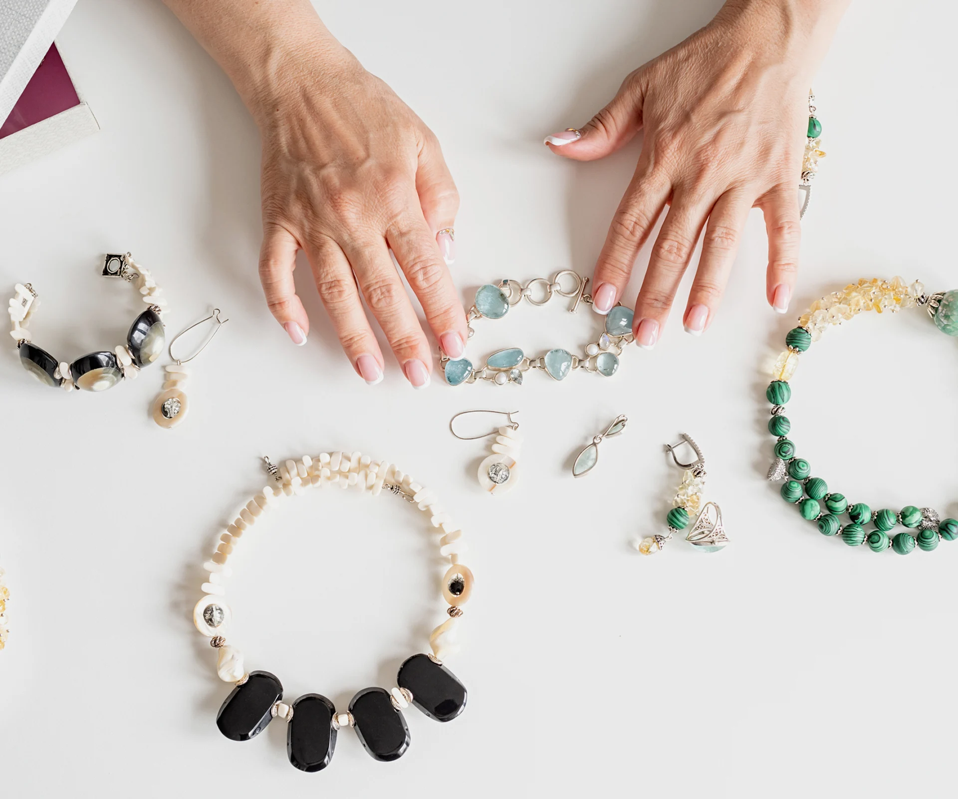 Hands arranging colorful jewelry on table.