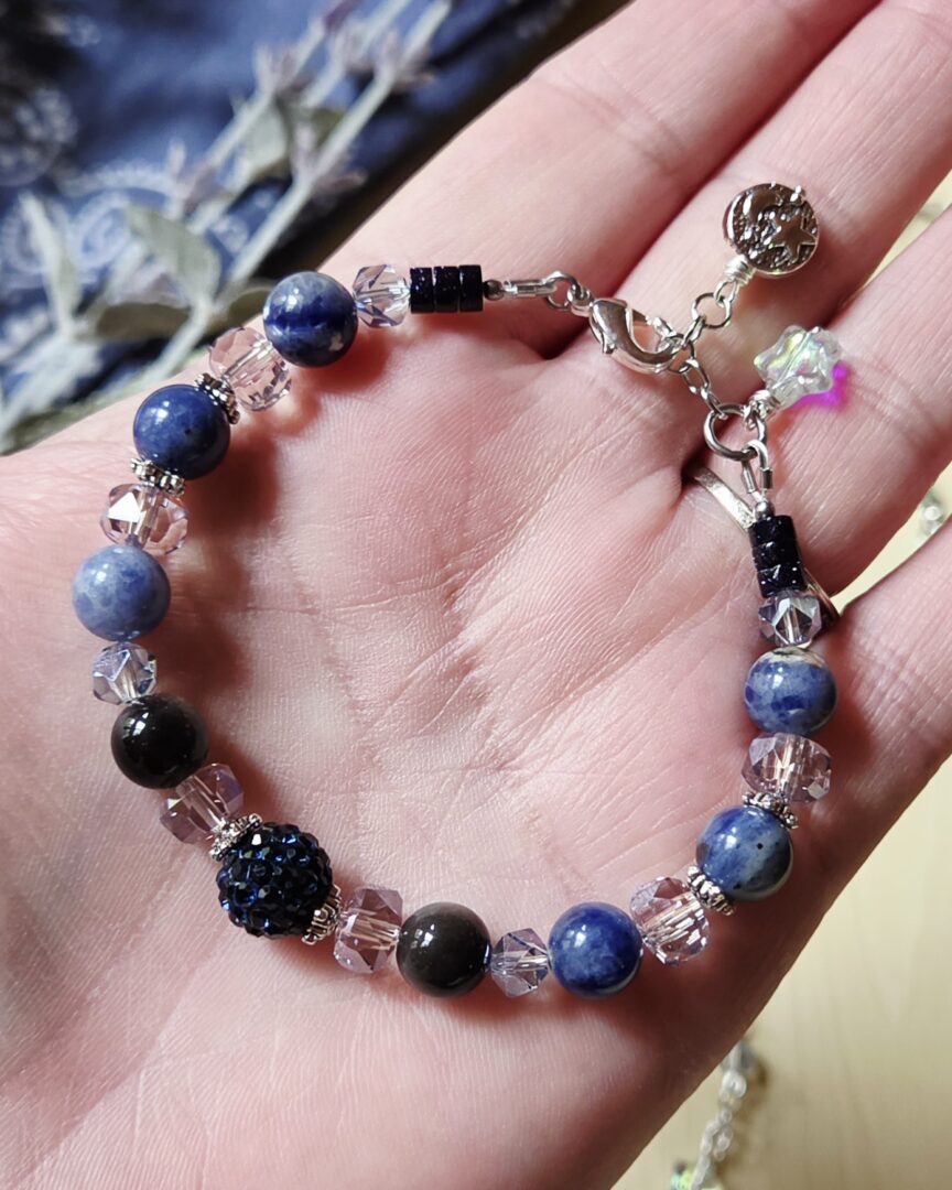 Stephanie holding a handmade silver sheen obsidian and sodalite bracelet with moon and star charms.