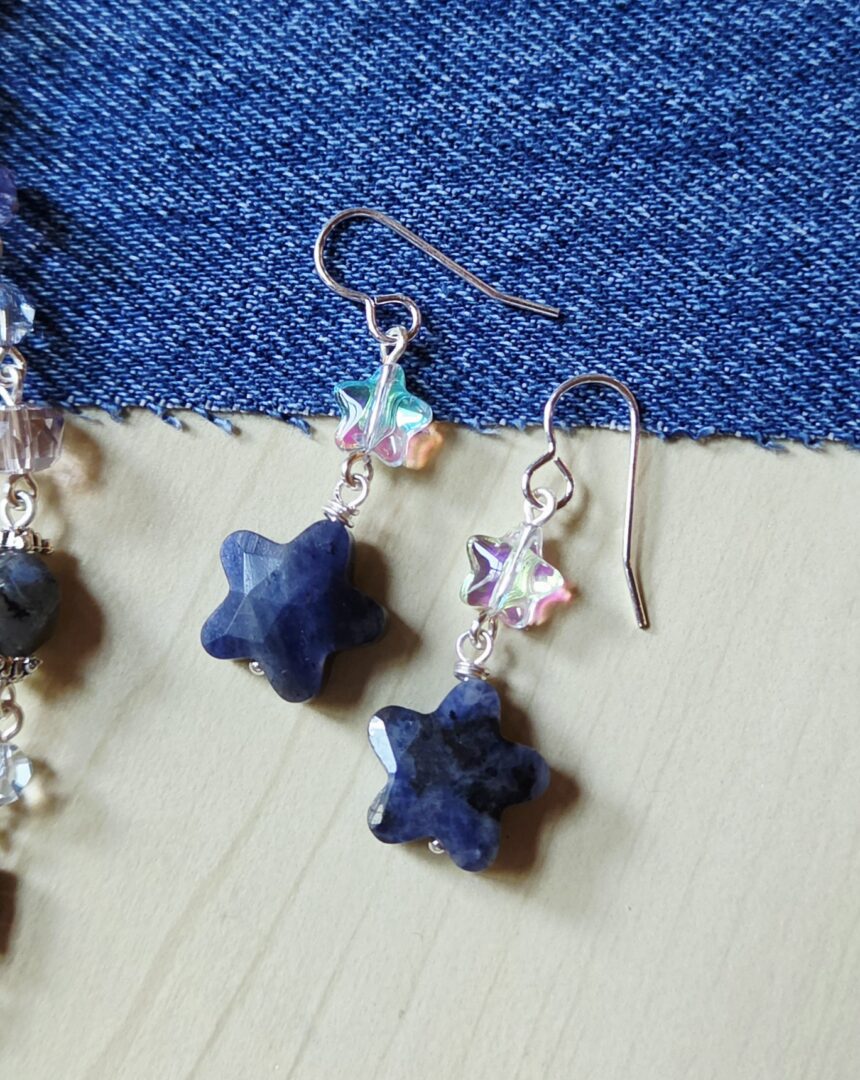 Close-up of handmade Sodalite Gemstone Star Earrings from Indigo Dusk, featuring iridescent crystal AB glass star beads paired with faceted blue sodalite gemstone star charms and silver earring wires.