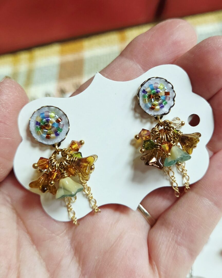 Floral dangle earrings with Swarovski crystals, featuring hand-stitched white felt seed bead earring posts, amber and bronze bell flowers, turquoise and cream accents, and gold chain details.