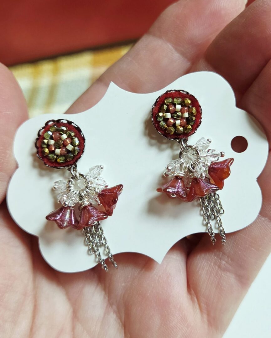 Floral dangle earrings with Swarovski crystals, featuring hand-stitched on maroon felt seed bead earring posts with frosted ruby Czech glass bell flowers, and delicate silver chain details.